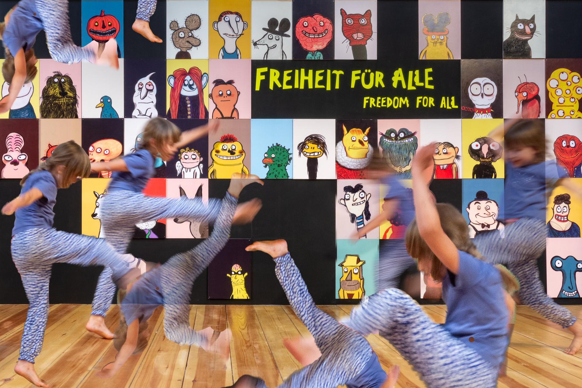 Ein Kind mit braunen Haaren und blauer Kleidung tobt vor dem Poster der Ausstellung "Freiheit für alle" des MACHMIT! Museums für Kinder.