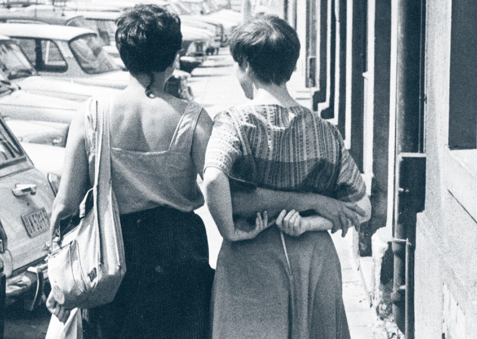 Eine Schwarzweiß-Fotografie von zwei Frauen, die Arm in Arm laufen.