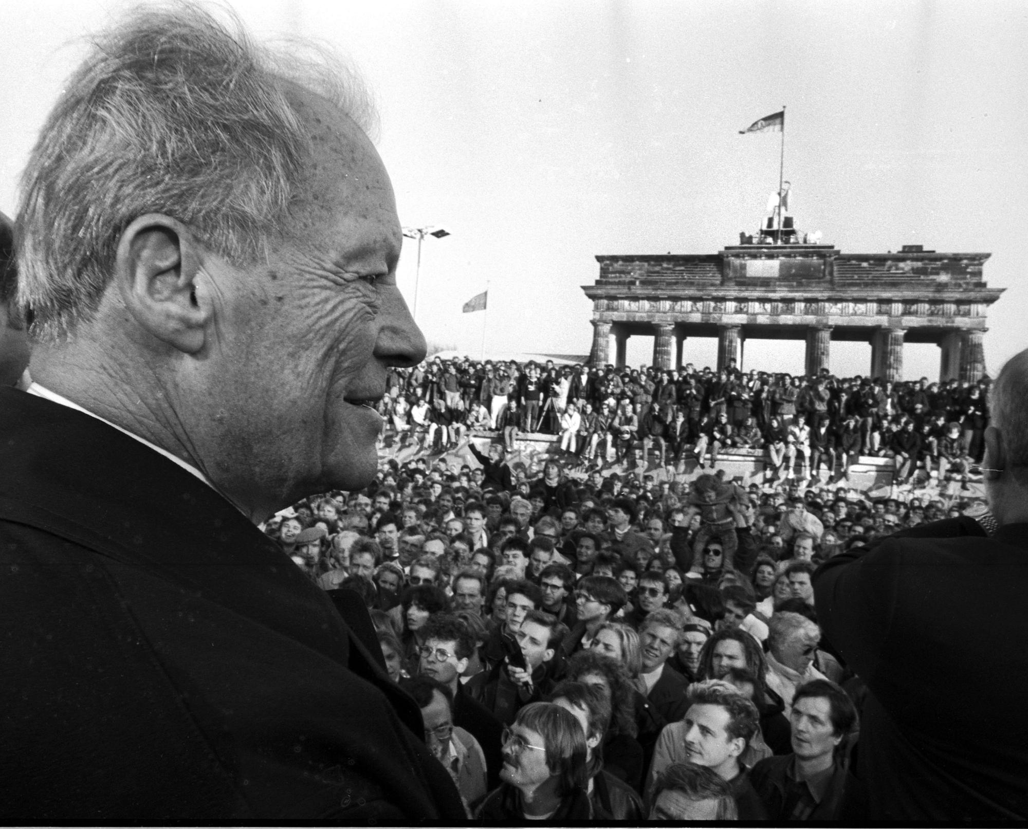 Ein Foto von Willy Brandt vor einer Menschenmenge am Brandenburger Tor.