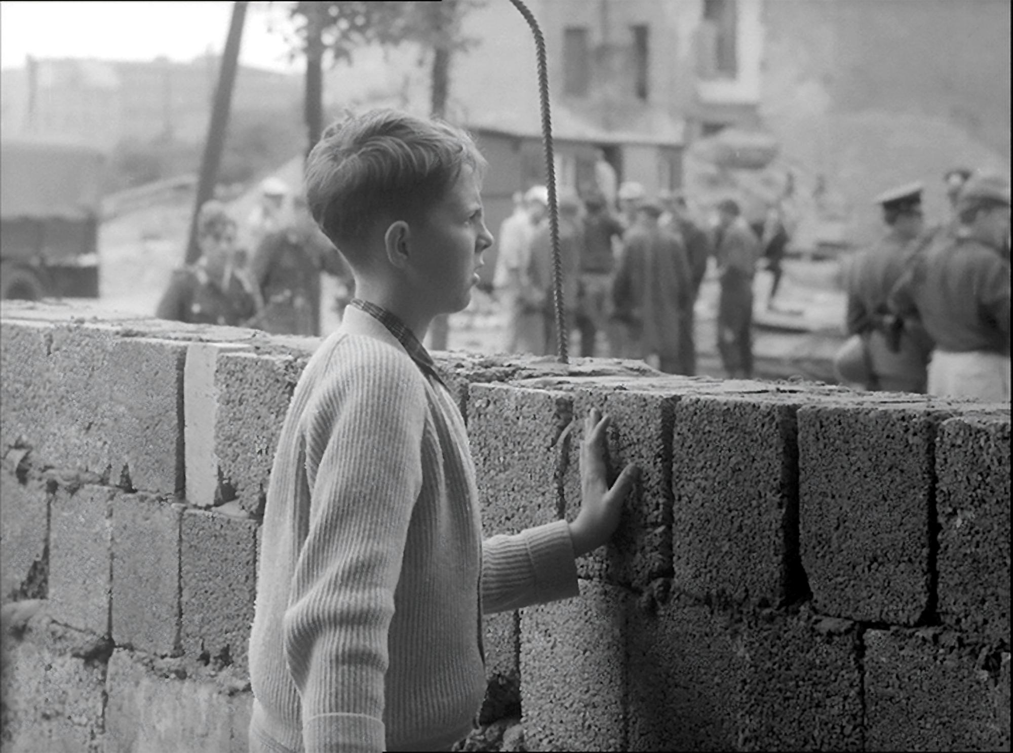 Filmstill: Ein Junge steht vor einer Mauer.