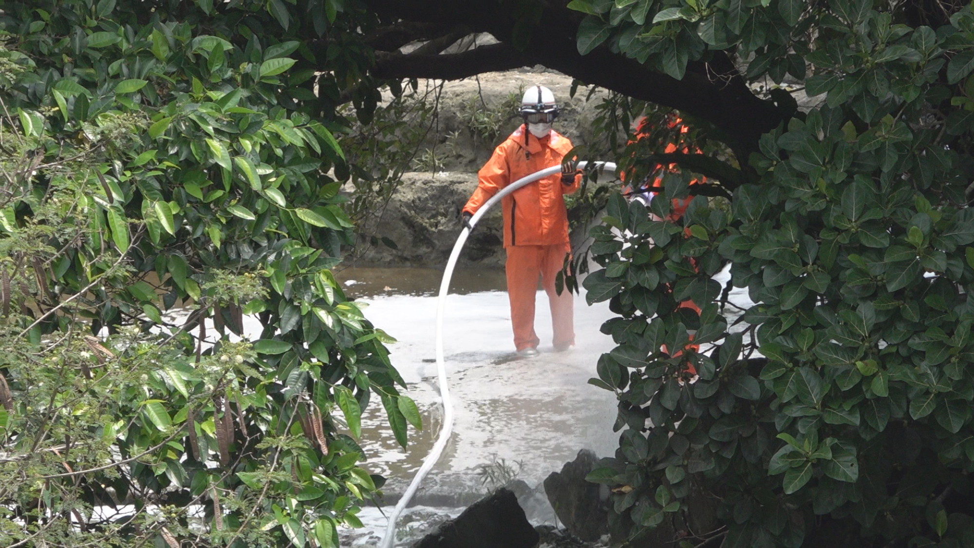 Ein Filmstill: Eine Person in orangener Schutzkleidung steht in einem Fluss.