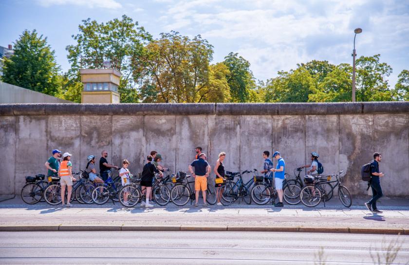 Die ehemalige Berliner Mauer mit Fahrrädern und Fahrradfahrern davor.