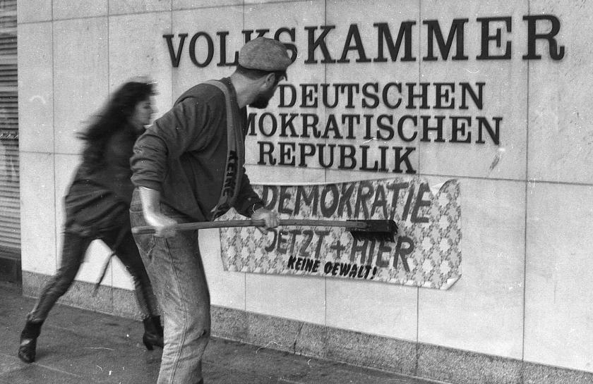 Zwei Demonstranten streichen eine neue Tapete unter das Schild der Volkskammer der DDR während der Alexanderplatz-Demonstration am 4. November 1989 in Ost-Berlin. Auf der Tapete steht "Demokratie jetzt und hier".