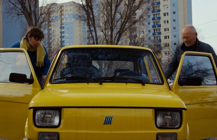 Ein Filmstill aus dem Film "Die noch unbekannten Tage": Zwei Menschen steigen in ein gelbes Auto aus DDR-Zeiten ein.