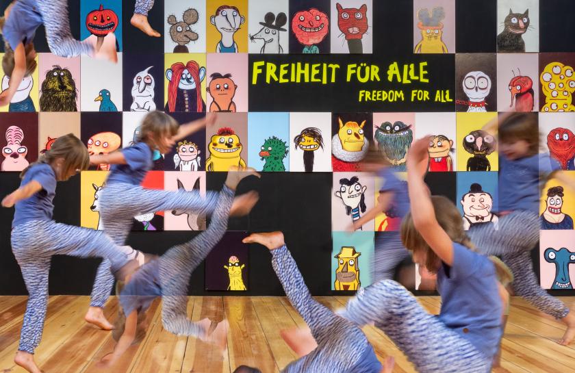 Ein Kind mit braunen Haaren und blauer Kleidung tobt vor dem Poster der Ausstellung "Freiheit für alle" des MACHMIT! Museums für Kinder.
