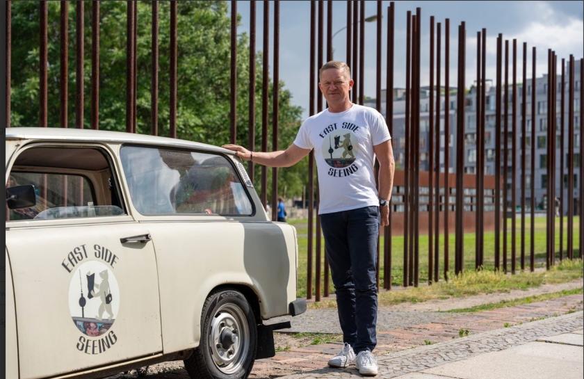 Ein Foto von Markus Wiehler vor der Gedenkstätte Berliner Mauer, mit einem alten Trabi-Auto.